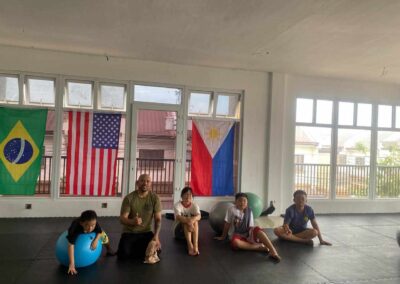 Professor Armand Panganiban of Philippine Top Team giving a shaka sign while posing with four young students on the gym mats after a kids' martial arts class.